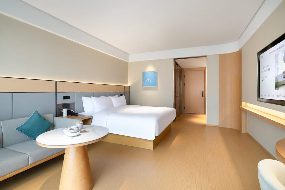 A modern hotel room with a bed, a sofa, a round table, and a TV screen.