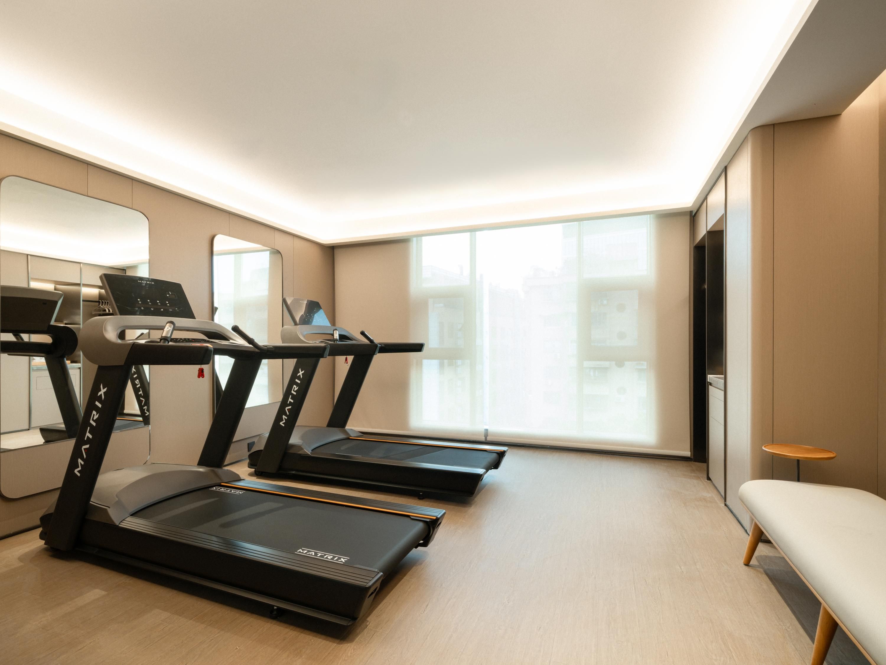 A modern hotel room with a treadmill, a large window, and a minimalist design.