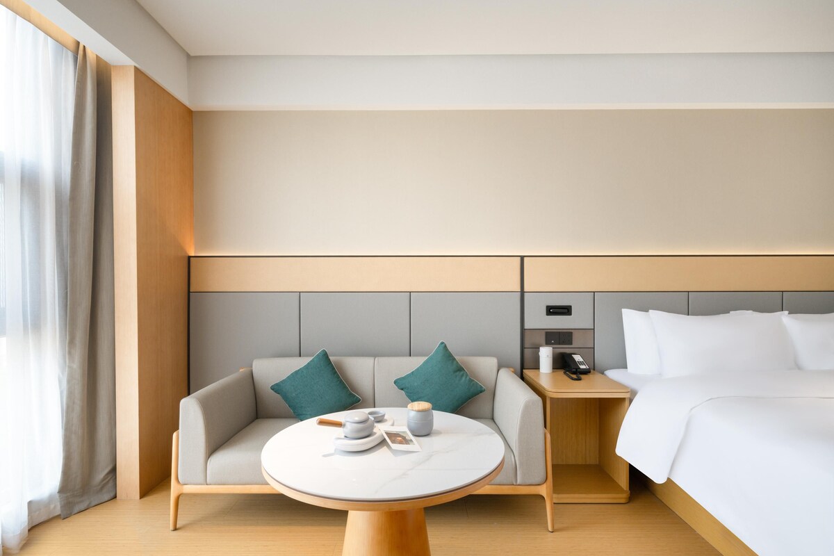 Una habitación de hotel moderna con cama, sofá, una mesita y una mesilla de noche.