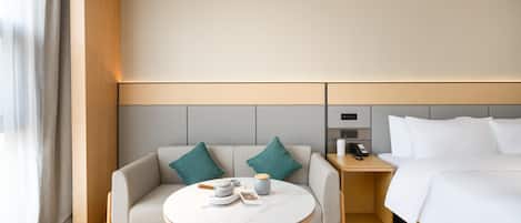 A modern hotel room with a bed, a sofa, a small table, and a nightstand.