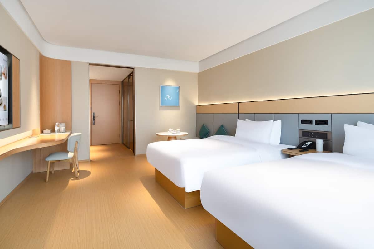 A modern hotel room with two beds, a desk, and a small table.