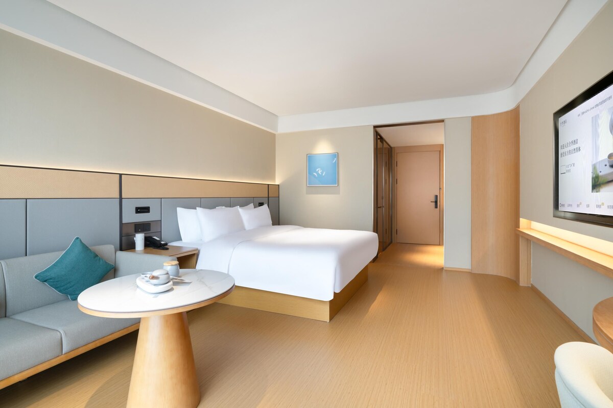 Una habitación de hotel moderna con una cama, un sofá, una mesa redonda y una pantalla de televisión.