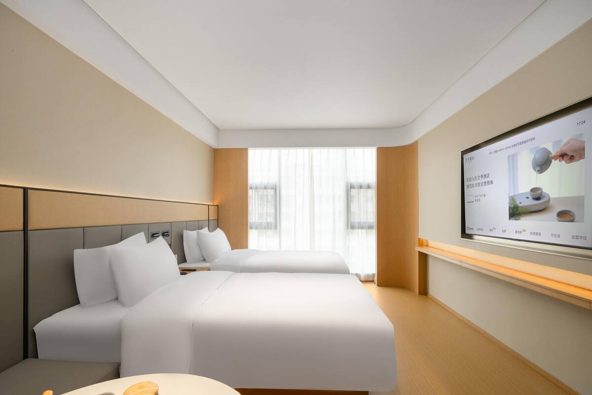 A hotel room with two beds, a TV on the wall, and a small table with cups and a teapot.