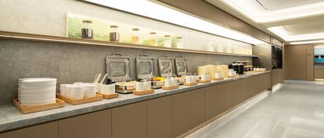 A modern breakfast bar with a long counter, stainless steel containers, and a variety of breakfast items.