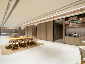 Un moderno vestíbulo de hotel con una recepción, un comedor con una mesa y sillas de madera, y una cocina con estantes y electrodomésticos.