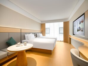 Una habitación de hotel moderna con una cama grande, una mesita redonda pequeña, un sofá y un televisor montado en la pared.