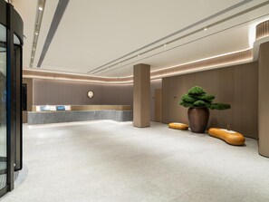 Un vestíbulo moderno con una recepción, una planta grande en maceta y un diseño minimalista.