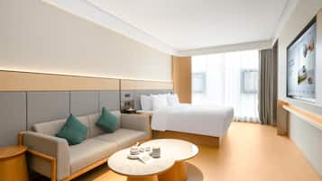 A modern hotel room with a sofa, a bed, a round coffee table, and a TV mounted on the wall.