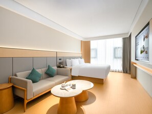 Una habitación de hotel moderna con sofá, cama, una mesita redonda y televisor montado en la pared.