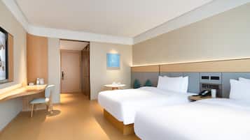 A modern hotel room with two beds, a desk, and a small table.