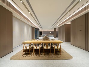 Una sala de conferencias moderna con una larga mesa y sillas, iluminación empotrada y una puerta de cristal que da a otra zona.