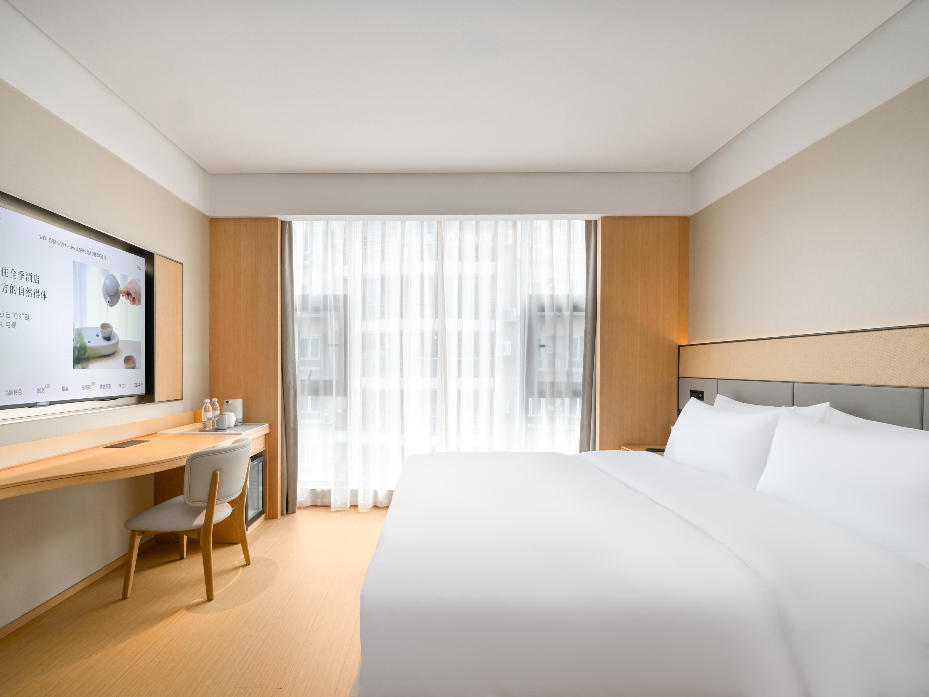 A hotel room with a bed, a desk, a chair, a TV, and a window with curtains.