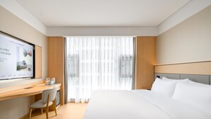 Een hotelkamer met een bed, een bureau, een stoel, een televisie en een raam met gordijnen.