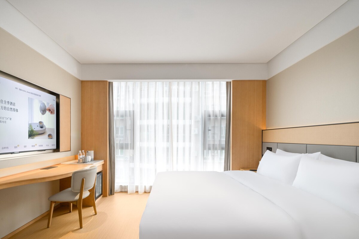 Een hotelkamer met een bed, een bureau, een stoel, een televisie en een raam met gordijnen.