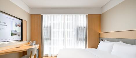 Quarto de hotel com cama, escrivaninha, cadeira, televisão e janela com cortinas.
