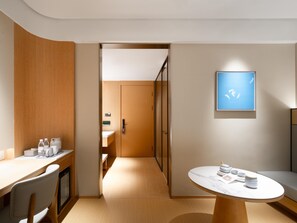 Una habitación de hotel moderna con un escritorio de madera, una mesa redonda con vajilla para té, un sofá y un cuadro enmarcado en la pared.