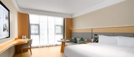A hotel room with a large bed, a desk with a chair, a small table, and a large window with curtains.