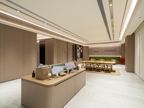 Un área de recepción moderna y bien iluminada con mostrador, asientos y un sofá verde al fondo.