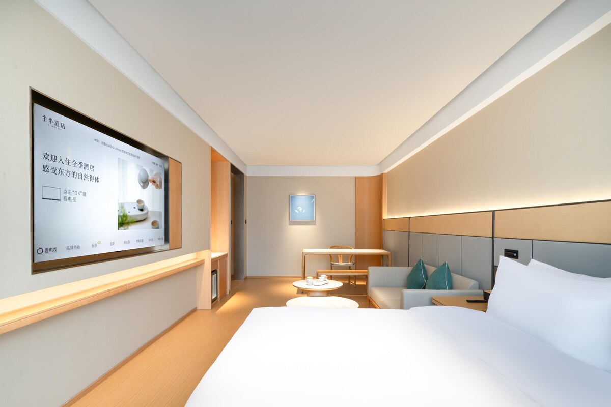 Una habitación de hotel moderna con una cama grande, un escritorio, una silla y un televisor montado en la pared.