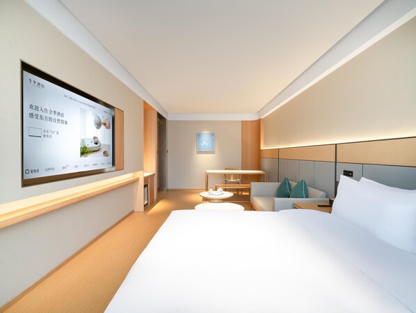 Una habitación de hotel moderna con una cama grande, un escritorio, una silla y un televisor montado en la pared.