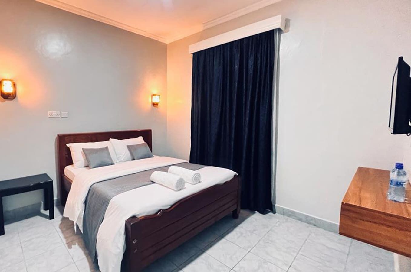 A hotel room with a bed, bedside table, and a mirror.
