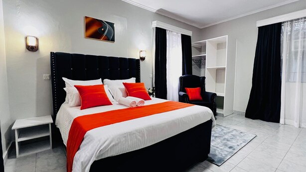 Une chambre d’hôtel moderne avec un grand lit, une petite table de chevet, une chaise et une étagère intégrée.