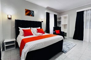 A modern hotel room with a large bed, a small bedside table, a chair, and a built-in shelf. - Maskan Guest House Kilimani Nairobi (Nairobi)