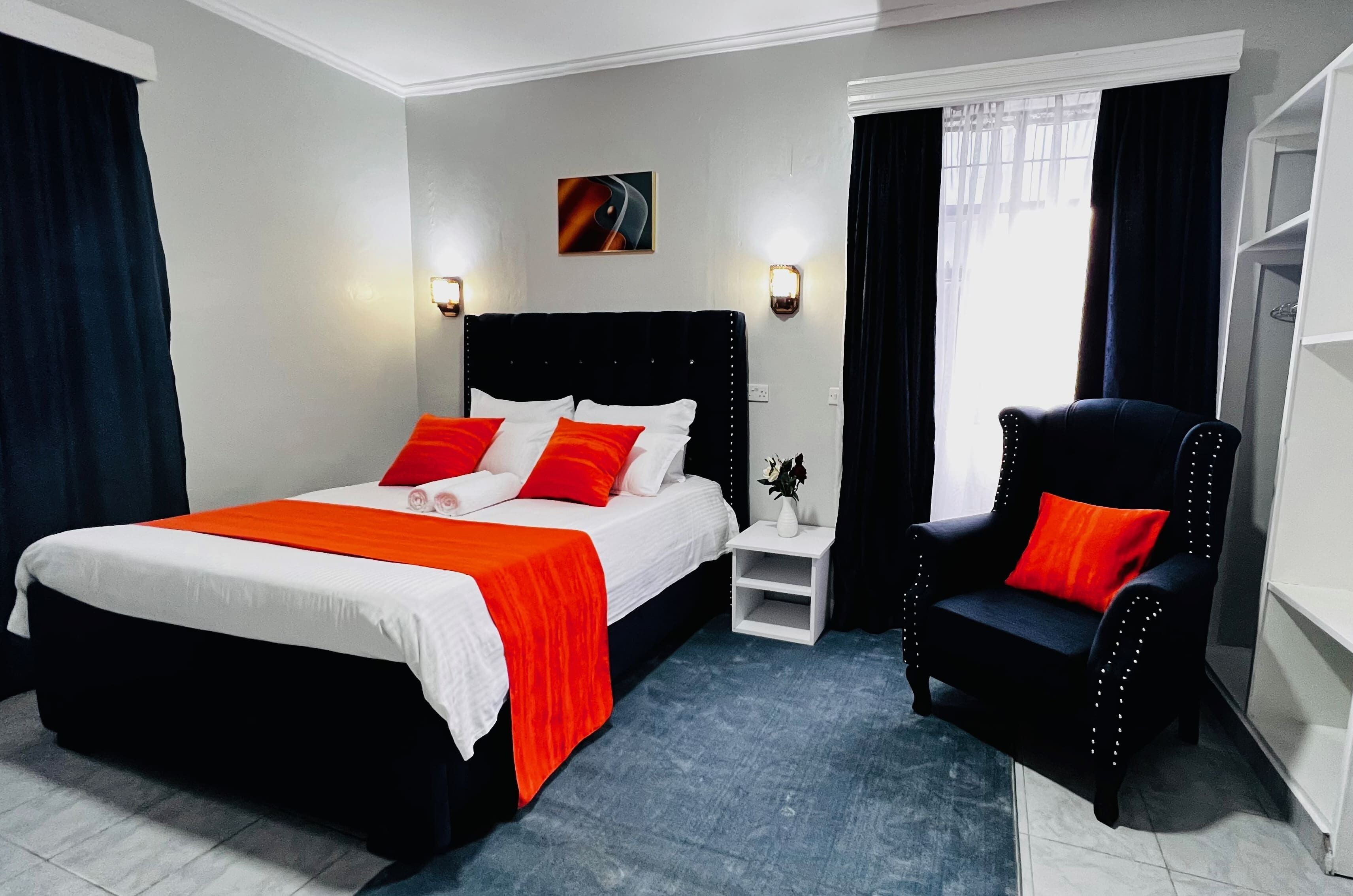 A hotel room with a bed, a chair, a nightstand, and a painting on the wall.