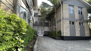 Un bâtiment moderne avec une allée en gravier, un petit jardin agrémenté de plantes et une porte blanche.