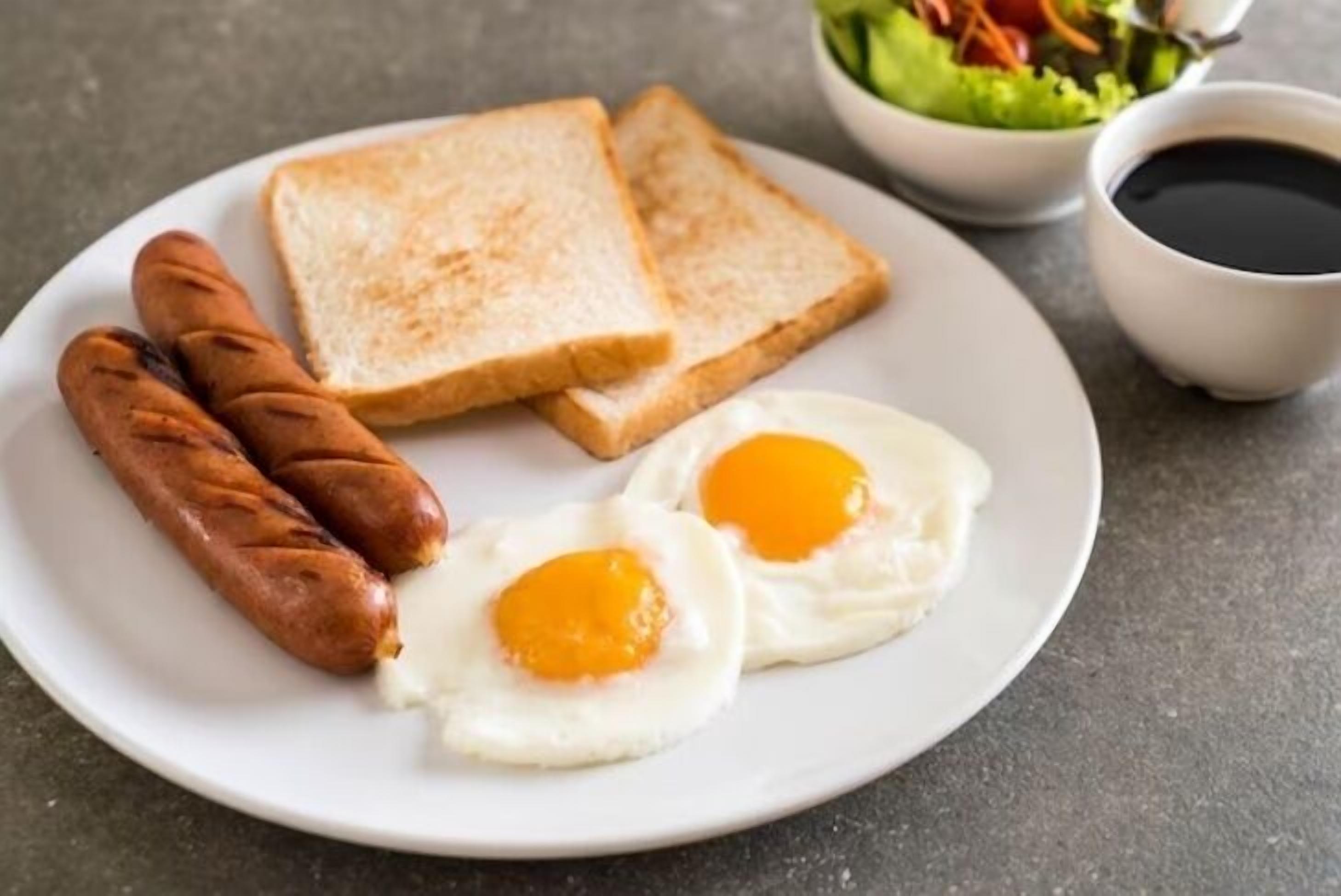 A plate with two fried eggs, two sausages, and two slices of toast on a table.