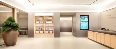 A modern reception area with a large potted plant, a wooden reception desk, and a digital display on the wall.