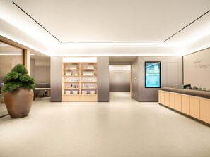 Ein moderner Empfangsbereich mit einer großen Küstpflanze, einem Holzbüro und einem digitalen Bildschirm an der Wand.