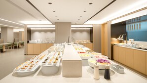A modern dining area with a long buffet table, seating area, and a counter with food items. - Ji Hotel Guangzhou Baiyun Airport Renhe Metro (Guangzhou)