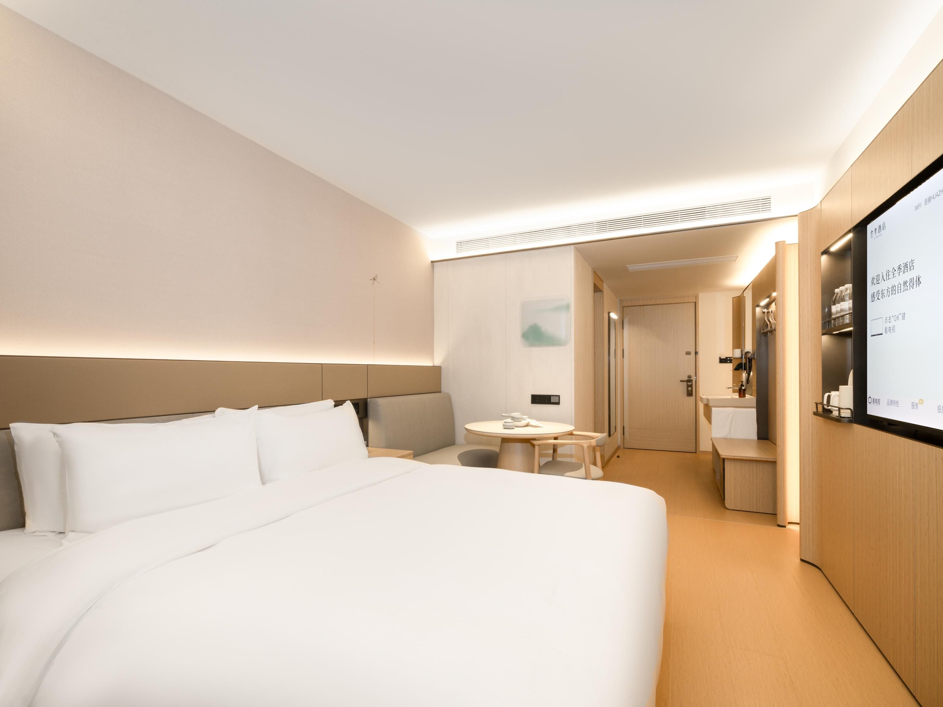 Quarto de hotel moderno com uma cama grande, uma mesa pequena e banheiro com espelho e pia.