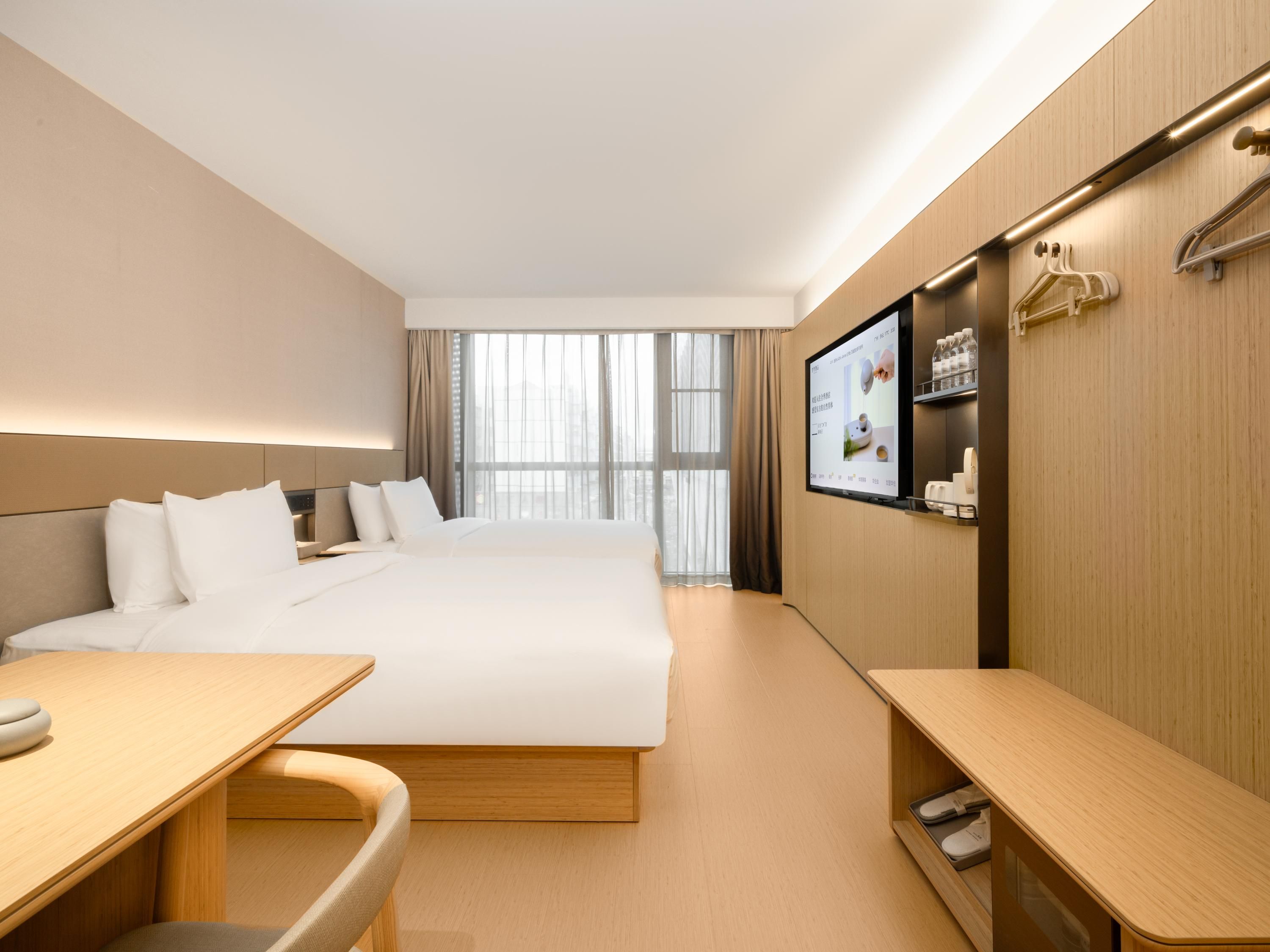 A modern hotel room with a large bed, a desk, a chair, a TV, and a shoe rack.