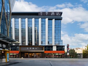 Un hôtel moderne, reconnaissable à son enseigne bien visible indiquant « JI HOTEL », et doté d’une grande entrée avec des portes en verre.