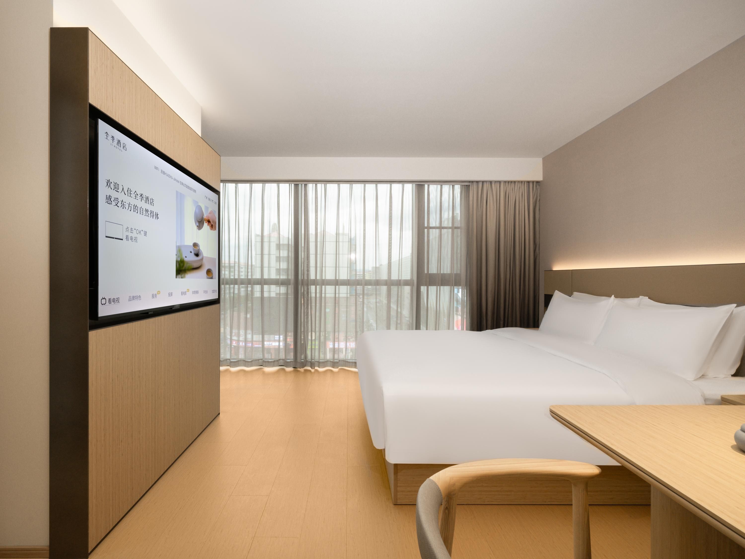 Quarto de hotel moderno com uma cama grande, uma escrivaninha e uma TV fixada na parede.