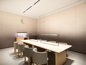 Uma sala de conferências moderna com uma mesa comprida, seis cadeiras, uma pequena escrivaninha com uma luminária e uma planta fixada na parede.