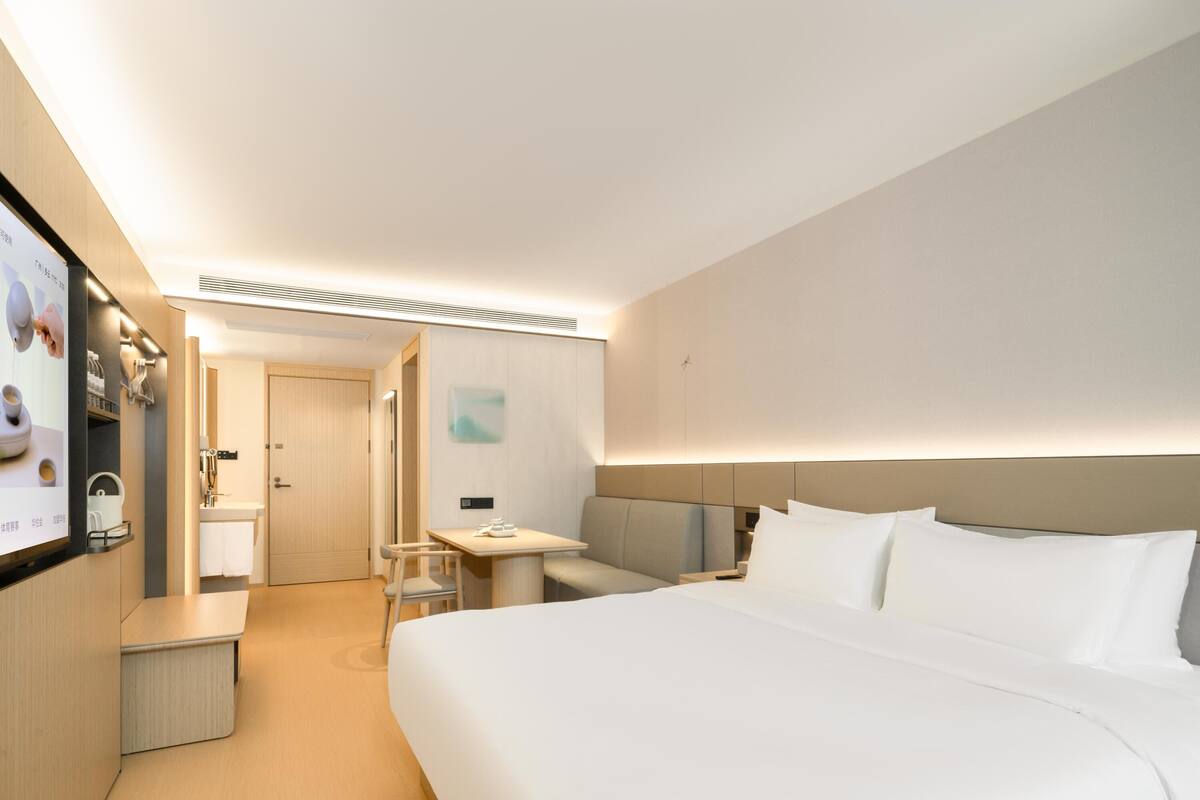 Una habitación de hotel moderna con una cama grande, una mesita de noche, un escritorio y un baño pequeño.