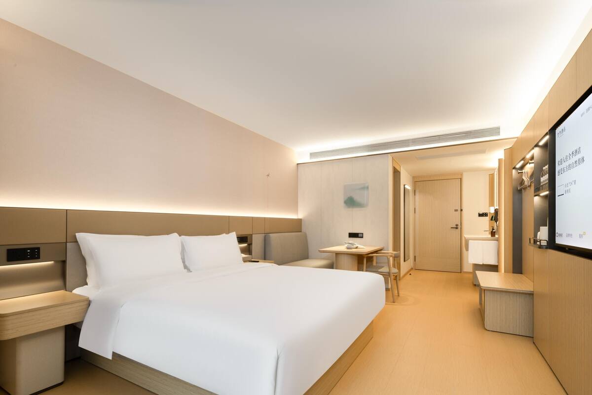 Una habitación de hotel moderna con una cama grande, mesitas de noche, un escritorio y un espejo.