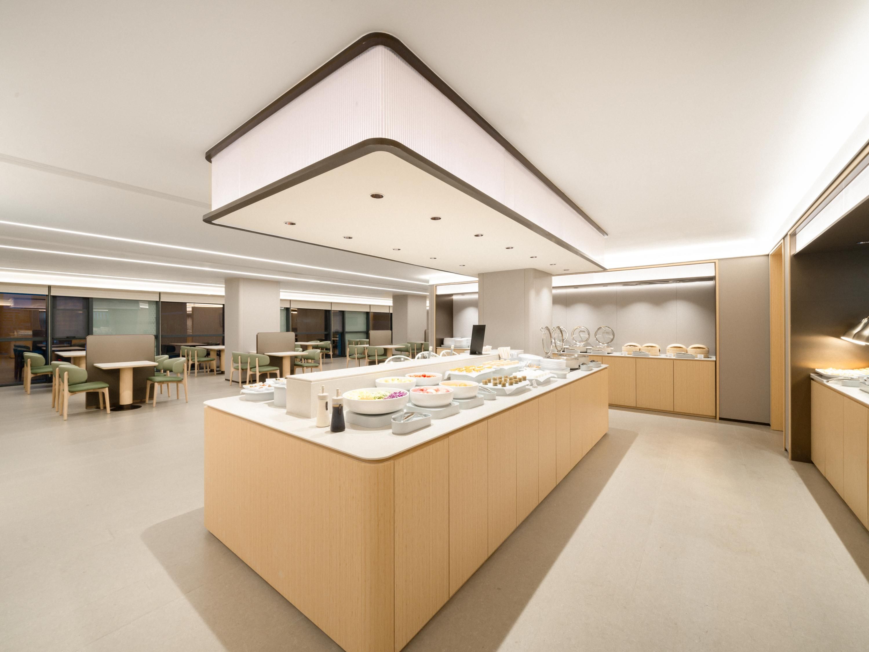 A modern, well-lit dining area with a central island featuring various food items and a seating arrangement of tables and chairs.