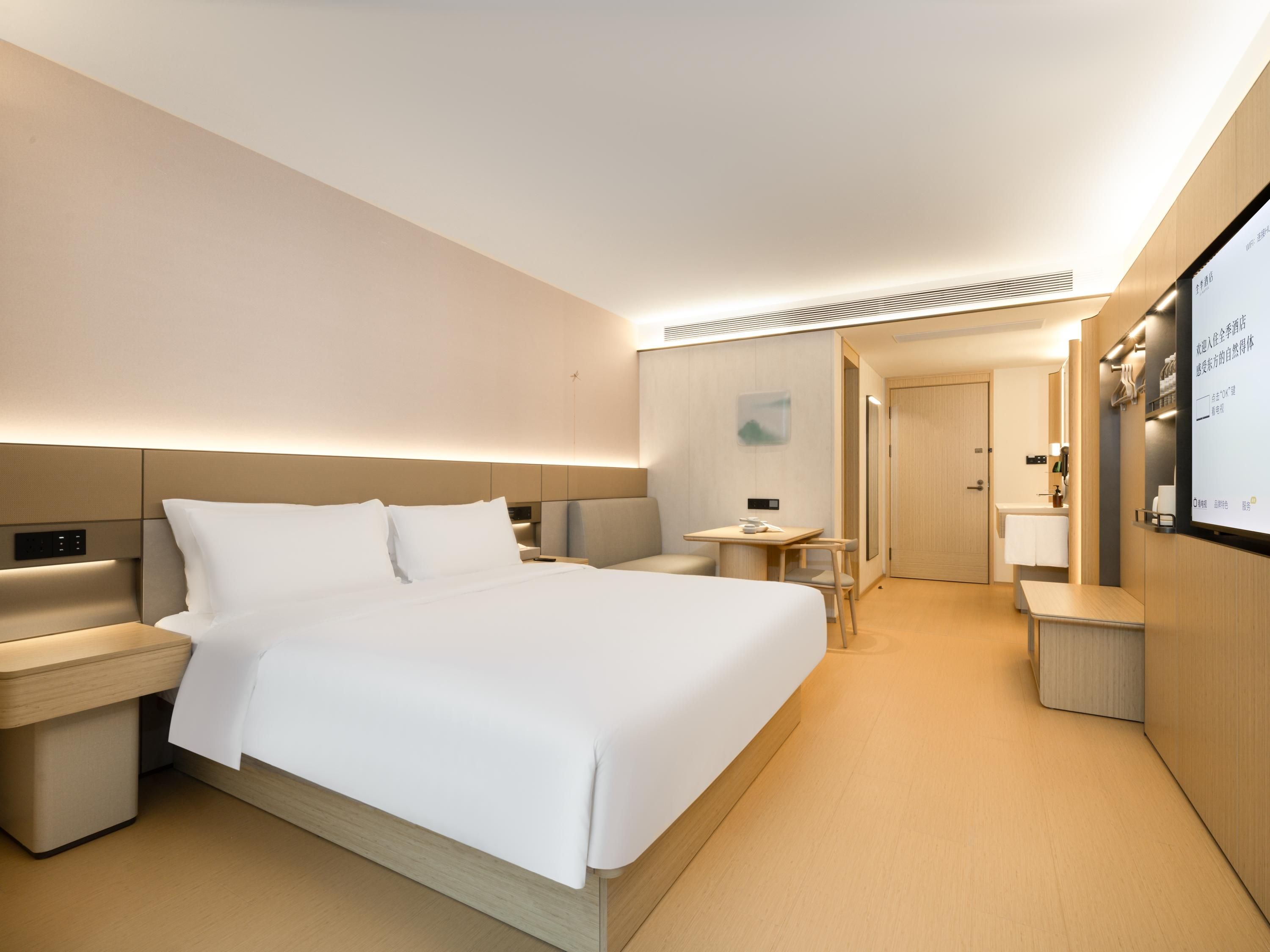 Quarto de hotel moderno com cama grande, mesas de cabeceira, escrivaninha e espelho.