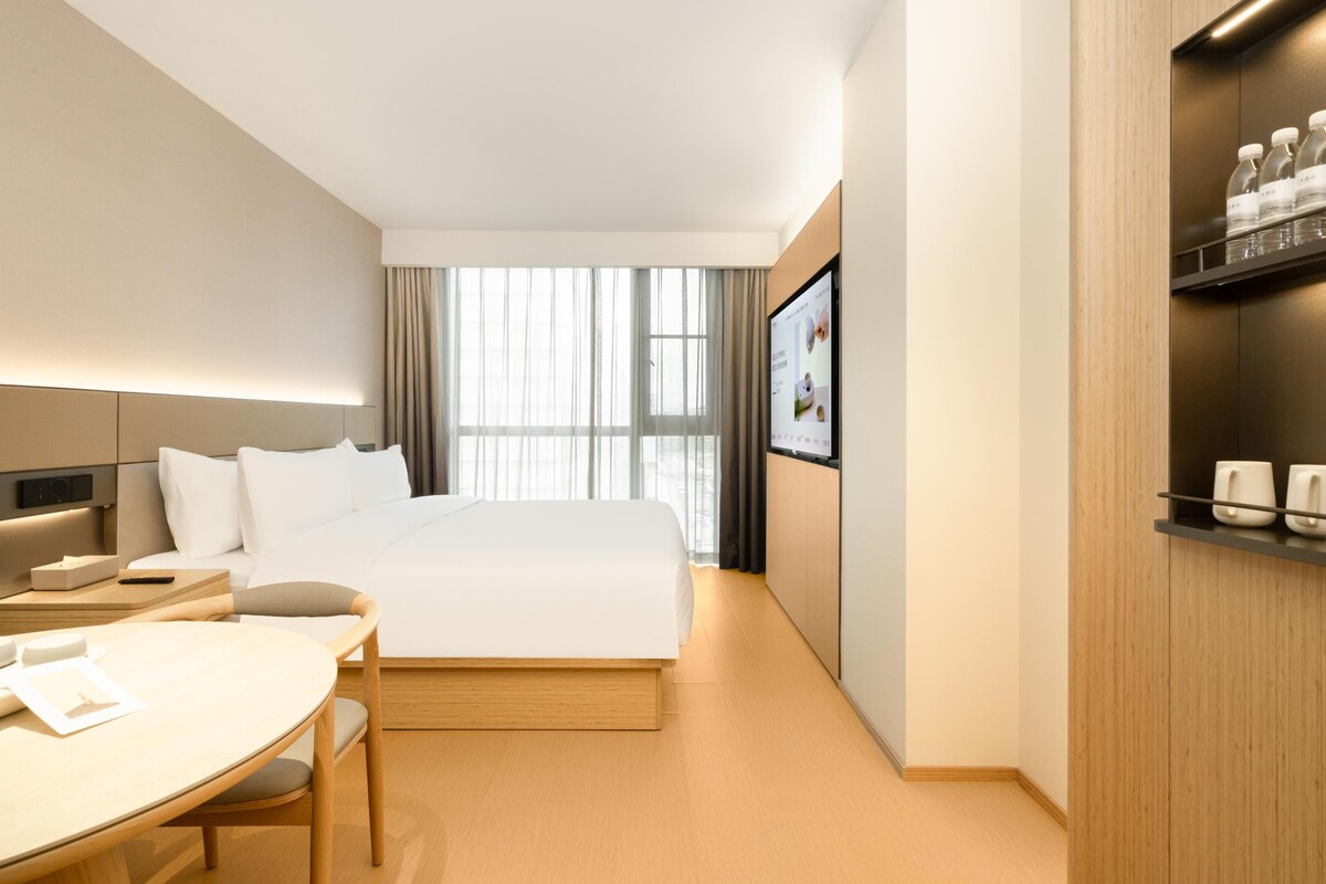 Ein modernes Hotelzimmer mit einem großen Bett, einem Schreibtisch und einem Fernsehbildschirm.