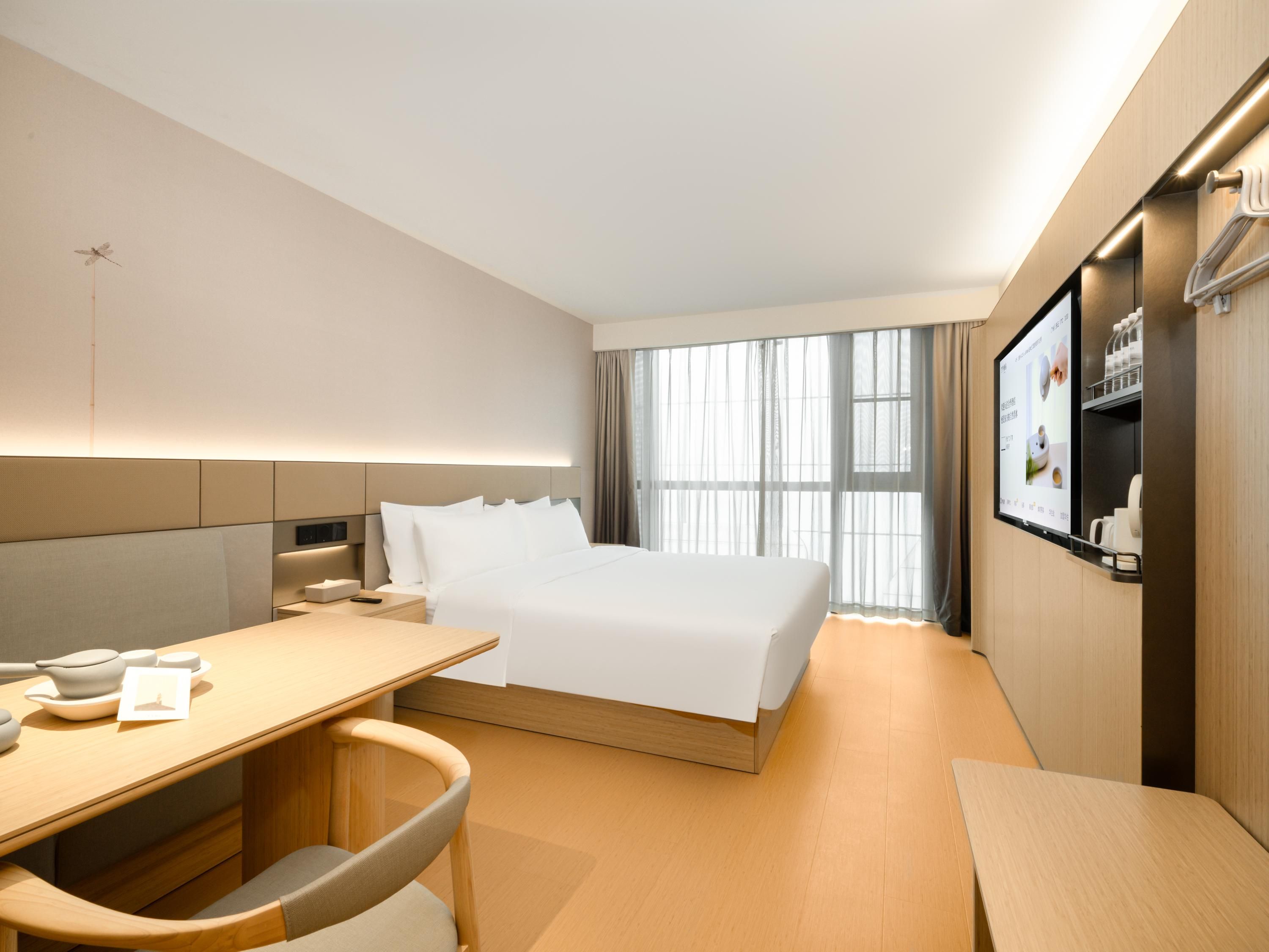 A hotel room with a bed, a desk, a chair, a TV, and a window with curtains.