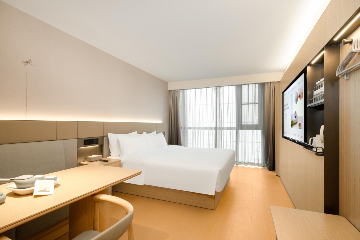 Ein Hotelzimmer mit Bett, Schreibtisch, Stuhl, Fernseher und einem Fenster mit Vorhängen.
