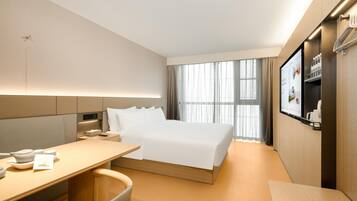 A hotel room with a bed, a desk, a chair, a TV, and a window with curtains.