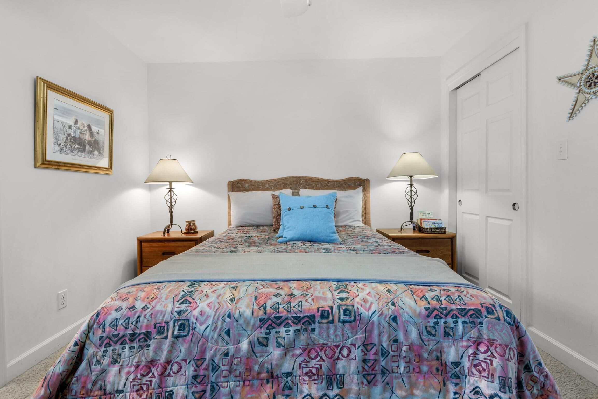 A bedroom with a bed, two bedside tables, a nightstand, a framed picture, and a door.