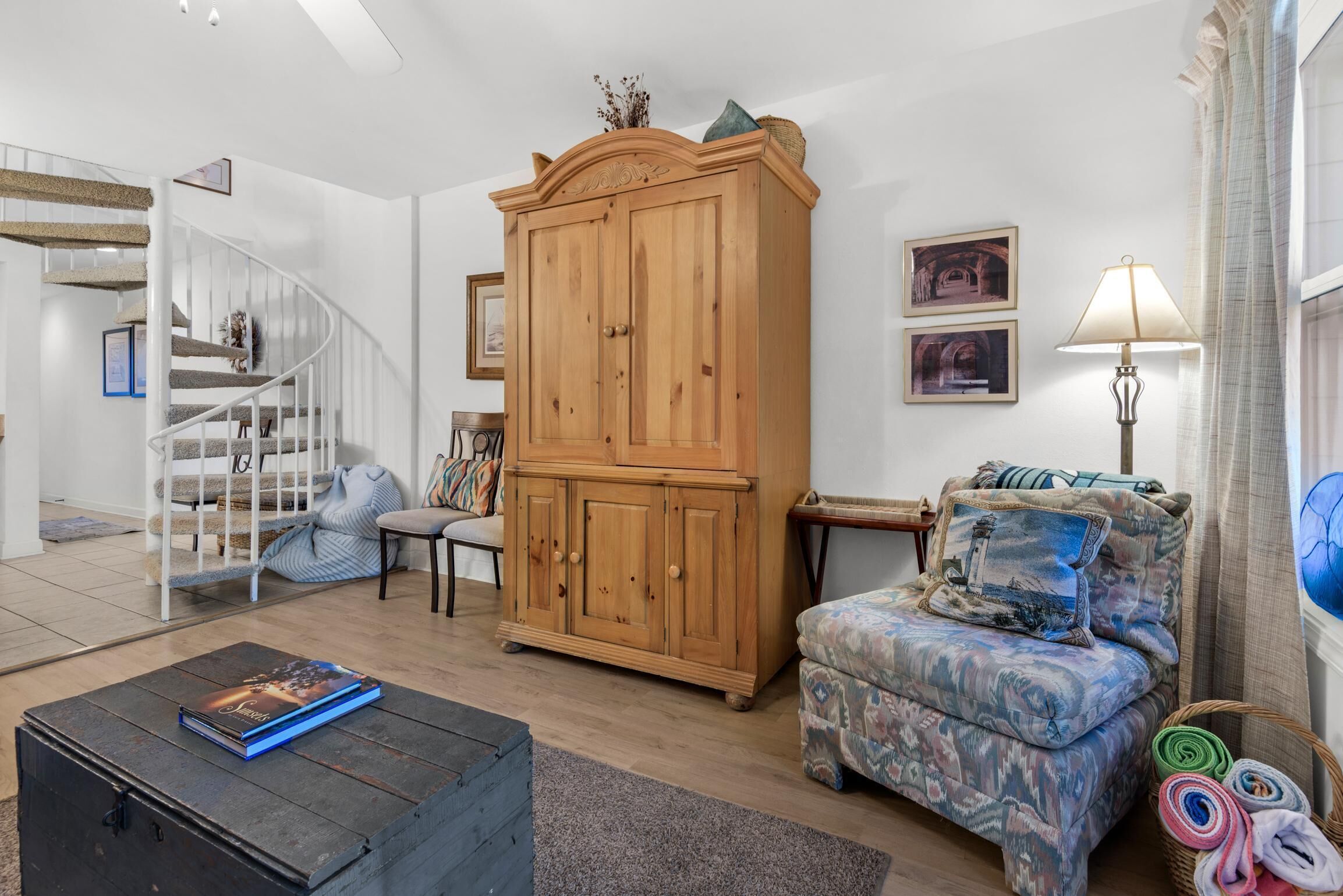 Una sala de estar con una escalera, un aparador de madera, un sillón estampado y una lámpara.