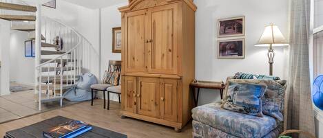 Una sala de estar con una escalera, un aparador de madera, un sillón estampado y una lámpara.