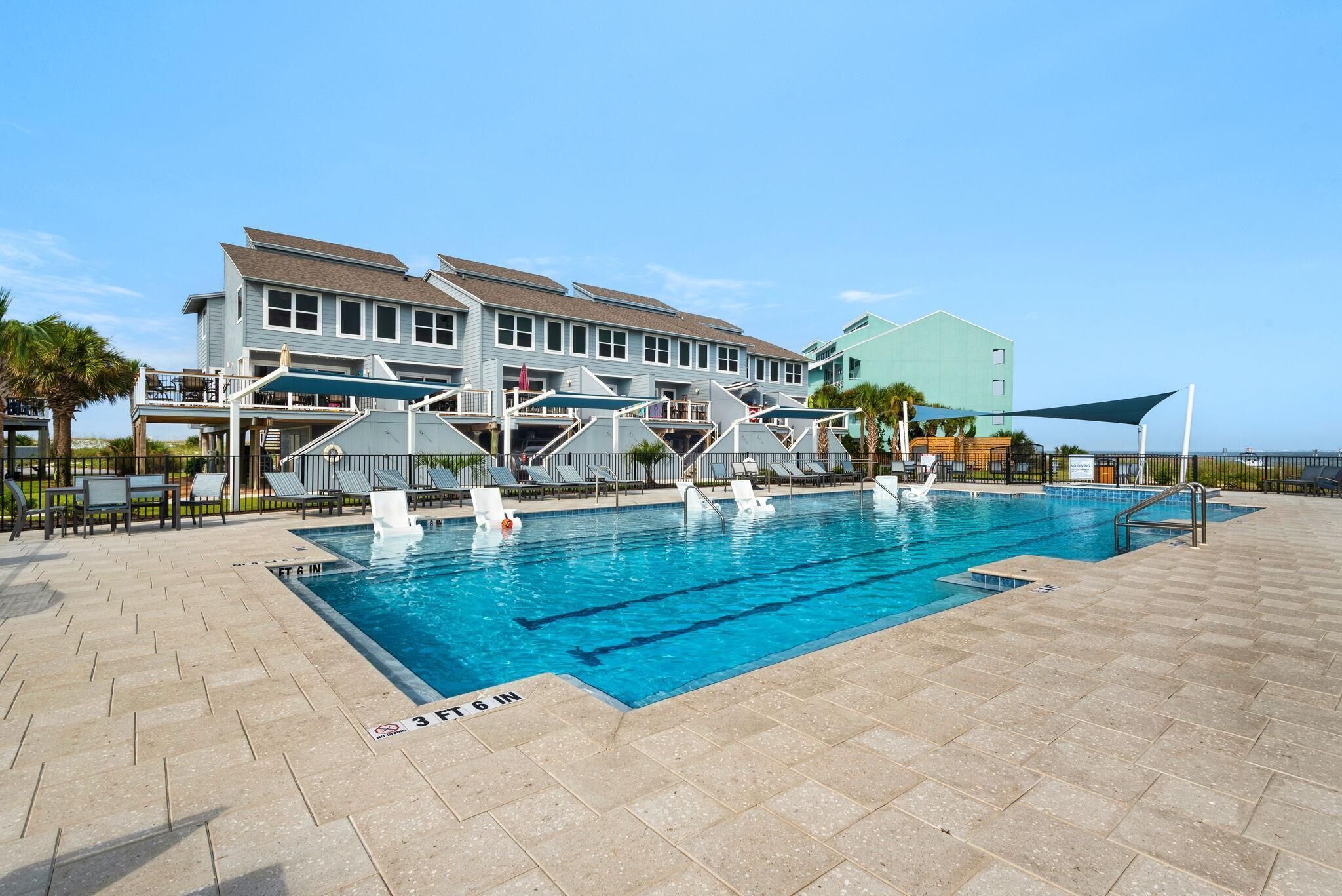 A swimming pool with a clear blue water, surrounded by lounge chairs and a building with multiple floors.